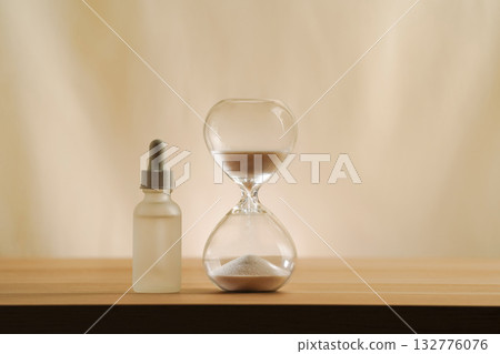 A modern still life featuring skincare product with an hourglass, embodying timeless beauty and minimalism. A focus on creativity and elegance in self-care displayed on a serene, neutral backdrop. 132776076