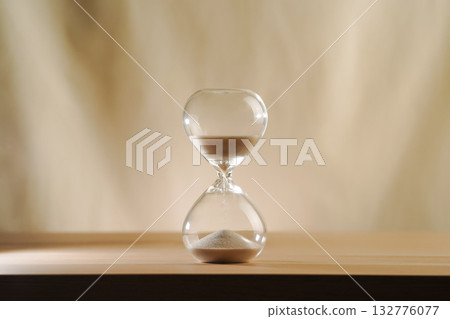 A simple hourglass on a wooden table with a beige backdrop, symbolizing time flow and minimalistic living. Represents timeless themes in a creative, uncluttered presentation for stylish concepts. 132776077