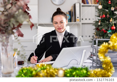 Portrait of successful business woman with New Years tinsel and Christmas tree in office 132776103