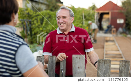 Two gardeners friendly talking outdoors next to wooden fence of country estate on day Two gardeners friendly talking outdoors next to wooden fence of country estate on day 132776105