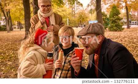 Family drinking tea and eating hotdogs together in autumn park Family drinking tea and eating hotdogs together in autumn park 132776111
