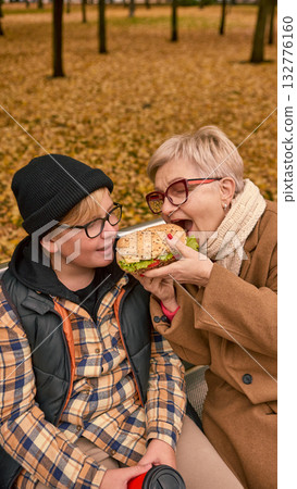 Grandmother sharing sandwich with grandson in autumn park 132776160