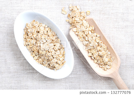 Rolled oats, thick-rolled and old-fashioned oats, in white bowl and grain scoop, on linen. Dehusked and steamed oat groats, rolled into flakes under heavy rollers, stabilized through lightly toasting. 132777076