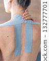 Close up view of young woman with kinesiology tape applied to her neck and shoulder holding her neck with her hand. Physical therapy and muscle recovery through modern rehabilitative care 132777701