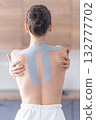 Young woman with kinesiology tape on her back and shoulders, embracing herself with both hands. Physical therapy, body awareness and emotional self-care through healing touch 132777702