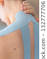 Close up view of young woman with kinesiology tape applied to her neck and shoulder holding her neck with her hand. Physical therapy and muscle recovery through modern rehabilitative care 132777706