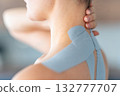 Close up view of young woman with kinesiology tape applied to her neck and shoulder holding her neck with her hand. Physical therapy and muscle recovery through modern rehabilitative care 132777707