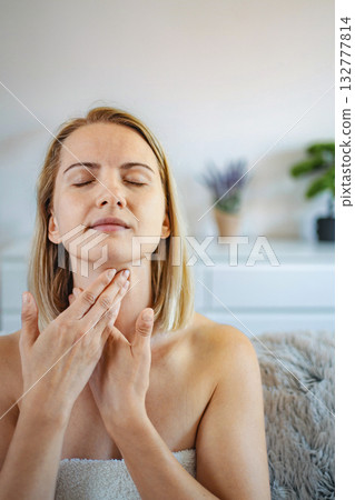 Woman gently massaging her neck with closed eyes, enjoying a moment of self-care at home 132777814