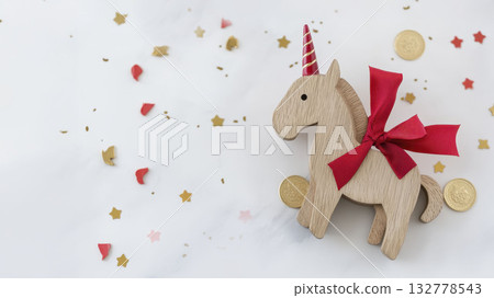 Festive wooden unicorn toy with red ribbon and gold coins on white background Festive wooden unicorn toy with red ribbon and gold coins on white background 132778543