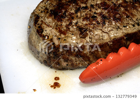 Close up of seasoned cooked steak resting on a white chopping board 132779349