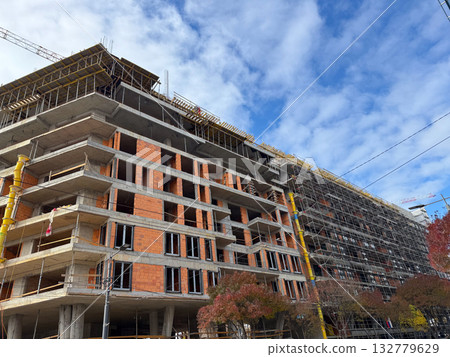 Large construction site with unfinished concrete building and scaffolding. Urban growth, infrastructure and architectural development in modern cities. Large construction site with unfinished concrete building and scaffolding. Urban growth, infrastructure and architectural development in modern cities. 132779629