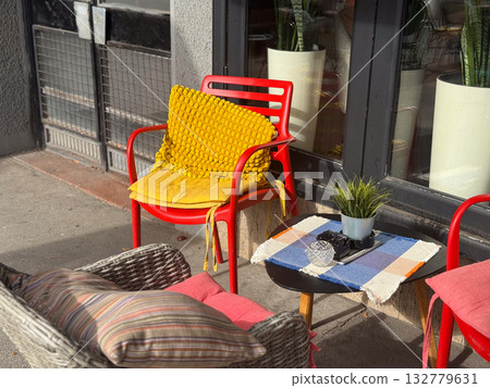 Colorful street cafe corner with red chair and yellow cushion in sunlight. Warmth, creativity and relaxed atmosphere in urban outdoor lifestyle. 132779631