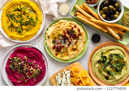 A vibrant spread showcases different types of hummus including classic, beetroot, broccoli, and turmeric. Accompanied by olives and breadsticks, it invites sharing and enjoyment A vibrant spread showcases different types of hummus including classic, beetroot, broccoli, and turmeric. Accompanied by olives and breadsticks, it invites sharing and enjoyment 132779809
