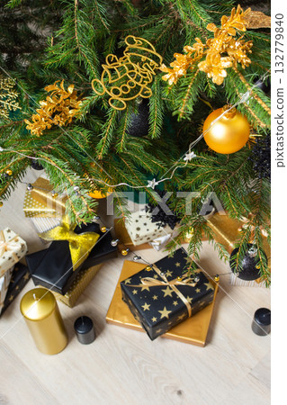 A festive scene featuring gold and black gift boxes, surrounded by shimmering candlelight and stylish decorations under a beautifully decorated Christmas tree, exuding elegance and charm 132779840