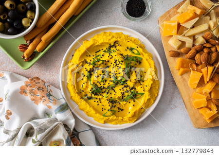 Gather around a colorful charcuterie board featuring turmeric hummus, cheese, nuts, and olives. This delightful spread invites friends to share tasty bites and enjoy each other company Gather around a colorful charcuterie board featuring turmeric hummus, cheese, nuts, and olives. This delightful spread invites friends to share tasty bites and enjoy each other company 132779843
