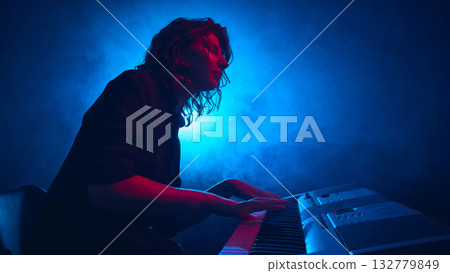 Musician performing at electronic keyboard with bright blue backlight 132779849