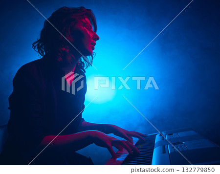 Female keyboardist playing under cinematic blue stage lighting Female keyboardist playing under cinematic blue stage lighting 132779850