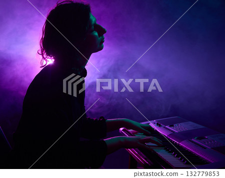Keyboard player performing on stage with purple haze lighting 132779853