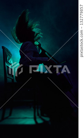 Female cellist silhouette performing with motion under dark teal light 132779857