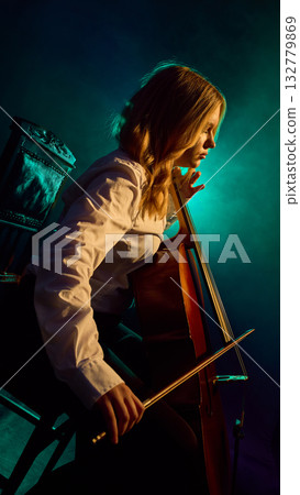 Side view of female cellist performing on stage with teal lighting 132779869