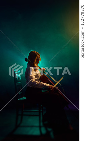 Classical cellist playing under dramatic teal and gold stage lights 132779870