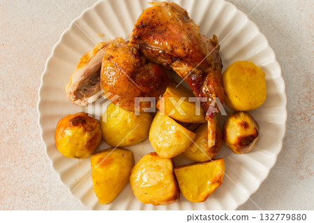 A delicious plate showcases a portion of baked rabbit alongside tender, golden roasted potatoes. The rabbit appears well-seasoned, with a crispy skin, while the potatoes are perfectly cooked A delicious plate showcases a portion of baked rabbit alongside tender, golden roasted potatoes. The rabbit appears well-seasoned, with a crispy skin, while the potatoes are perfectly cooked 132779880