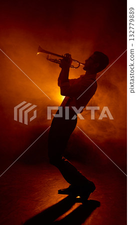 Trumpet player leaning back while performing under orange light 132779889