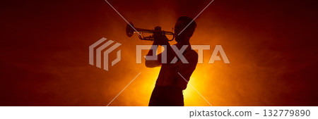 Trumpet player silhouette against warm concert lighting background. Banner 132779890