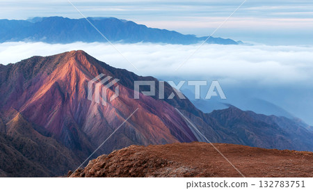 Stunning Red Mountain Peak Bathed in Warm Sunlight Above a Sea of Clouds and Vast Mountain Range Stunning Red Mountain Peak Bathed in Warm Sunlight Above a Sea of Clouds and Vast Mountain Range 132783751