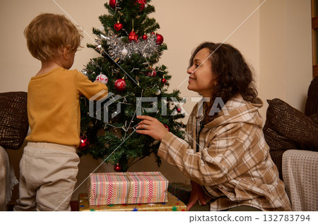 Mother And Child Decorating The Christmas Tree At Home With Gifts Underneath Mother And Child Decorating The Christmas Tree At Home With Gifts Underneath 132783794