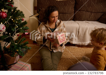 Mother Gifting a Present to Child by the Christmas Tree at Home 132783796