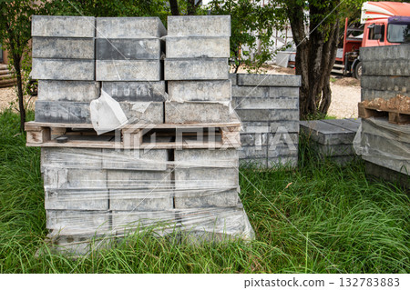Pile of gray concrete paving blocks neatly stacked on pallets and wrapped in plastic 132783883