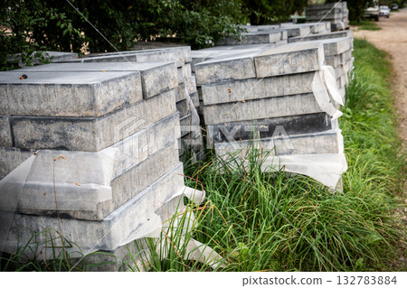 Multiple stacks of gray concrete paving blocks wrapped in protective material 132783884