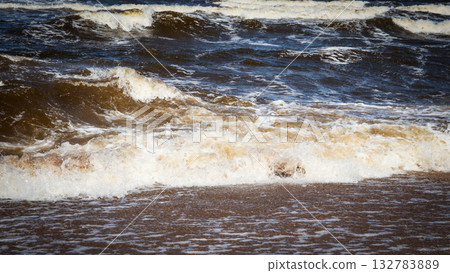 Dynamic view of powerful sea waves hitting the shore with foamy water Dynamic view of powerful sea waves hitting the shore with foamy water 132783889