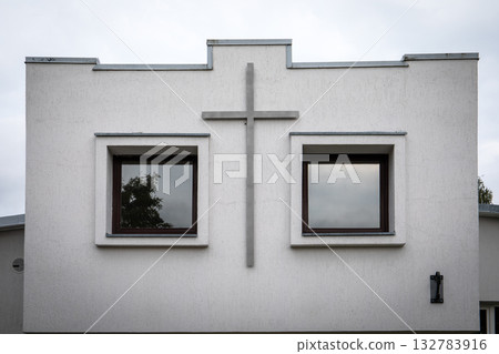 Front view of a minimalist church building facade featuring a large cross between two square windows Front view of a minimalist church building facade featuring a large cross between two square windows 132783916