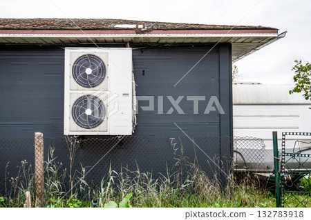 Large air conditioning outdoor unit with dual fans mounted on the exterior wall of a house Large air conditioning outdoor unit with dual fans mounted on the exterior wall of a house 132783918