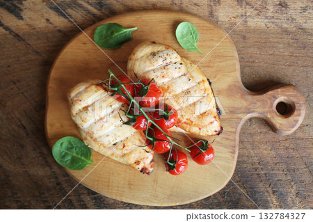Grilled chicken breast with cherry tomatoes on a wooden board. Traditional cuisine. Grill kitchen. Grilled chicken breast with cherry tomatoes on a wooden board. Traditional cuisine. Grill kitchen. 132784327