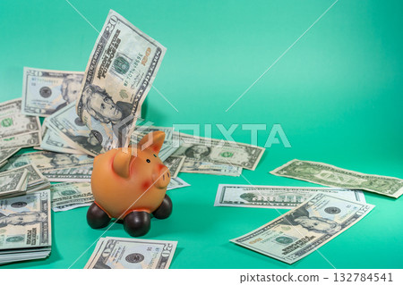 A piggy bank overflowing with cash, symbolizing saving and investment against a teal background. A piggy bank overflowing with cash, symbolizing saving and investment against a teal background. 132784541