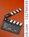 A classic clapperboard sits on a contrasting orange surface, ready for the next scene to be filmed. 132784548