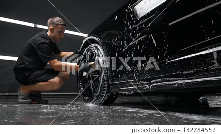 Technician washing car wheel during foam detailing in service bay 132784552