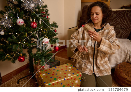 Woman Decorating Christmas Tree At Home With Gift Boxes And Cozy Holiday Atmosphere Woman Decorating Christmas Tree At Home With Gift Boxes And Cozy Holiday Atmosphere 132784679