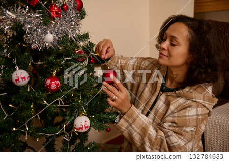 Woman Decorating Christmas Tree With Red Ornament In Cozy Living Room Woman Decorating Christmas Tree With Red Ornament In Cozy Living Room 132784683