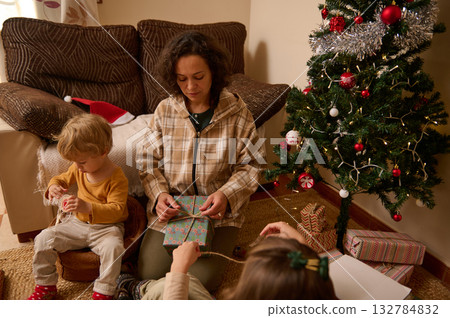 Cozy Family Christmas Eve Moment With Mother And Child Wrapping Gifts By The Tree 132784832