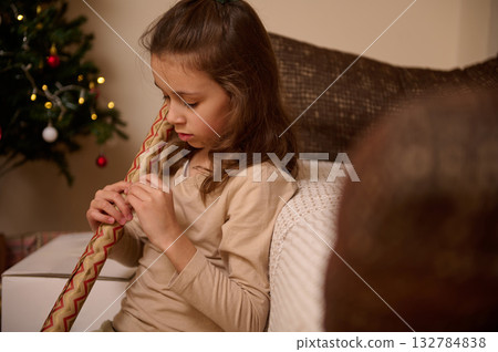 Young Girl Unwrapping a Christmas Gift on Couch with Tree in the Background 132784838