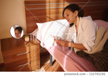 Woman Relaxing In Bed With Smartphone By Mirror And Nightstand At Home Woman Relaxing In Bed With Smartphone By Mirror And Nightstand At Home 132785292