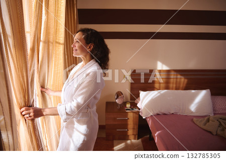 Woman In White Robe Looking Out The Window In A Hotel Room Morning Light 132785305