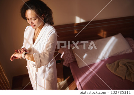 Woman In White Robe Checks Time In Morning Light By Bedside Woman In White Robe Checks Time In Morning Light By Bedside 132785311
