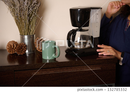 Cozy Kitchen Scene With Coffee Maker, Mug, Pinecones, And Dried Lavender On Dark Wood Counter Cozy Kitchen Scene With Coffee Maker, Mug, Pinecones, And Dried Lavender On Dark Wood Counter 132785332