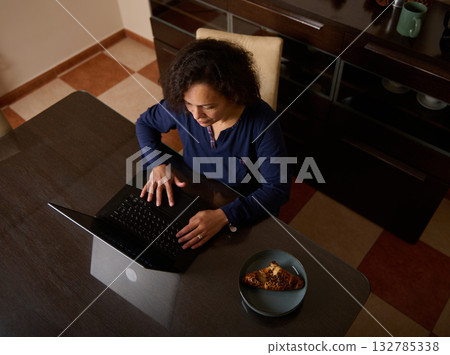 Woman Working On Laptop At Kitchen Table With Croissant Plate Nearby 132785338