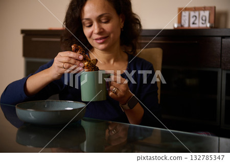 Woman Enjoying Cookie and Coffee at Kitchen Table, Cozy Morning Moment 132785347